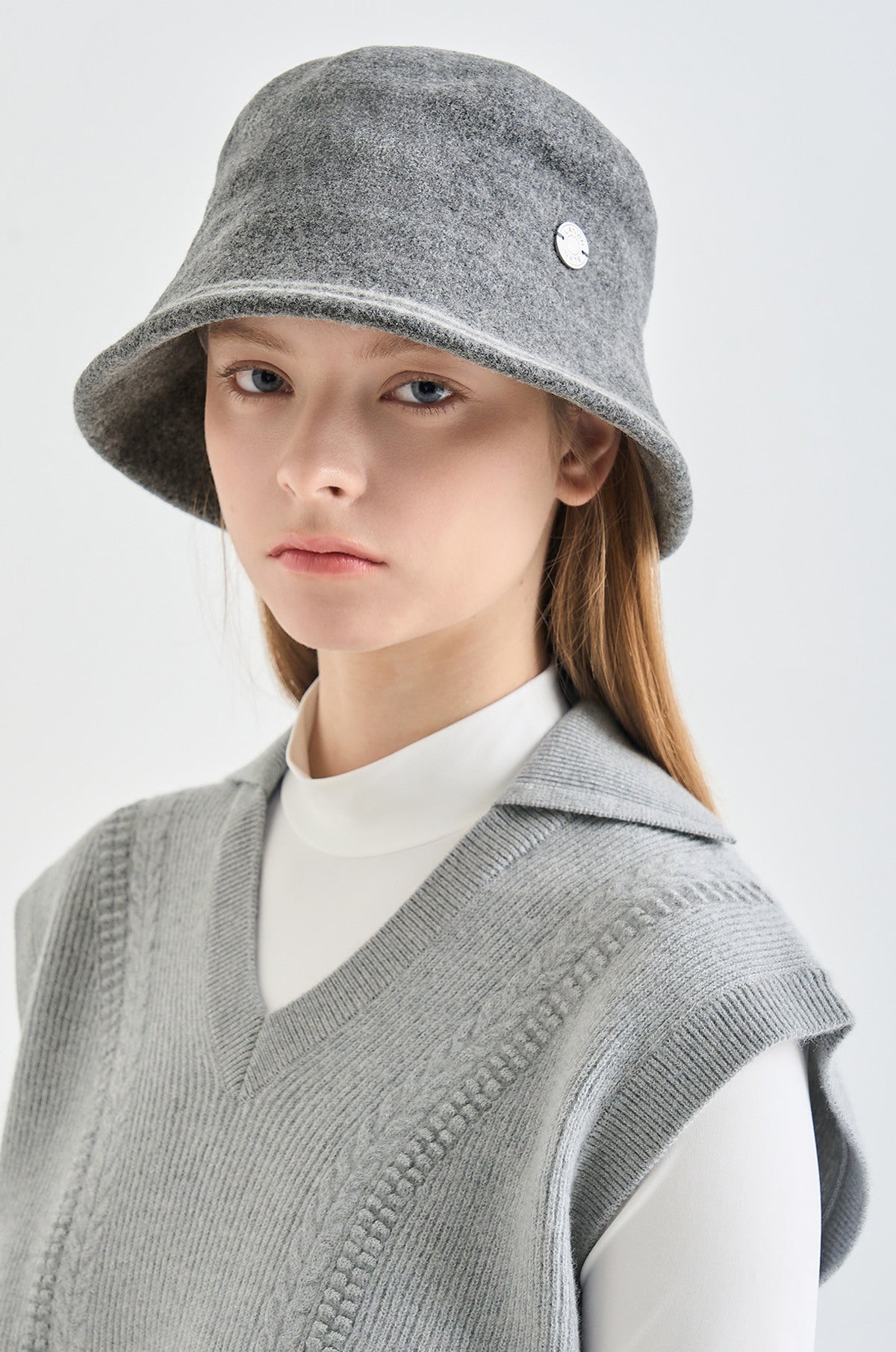 Person wearing a gray bucket hat and knitted vest on a white background