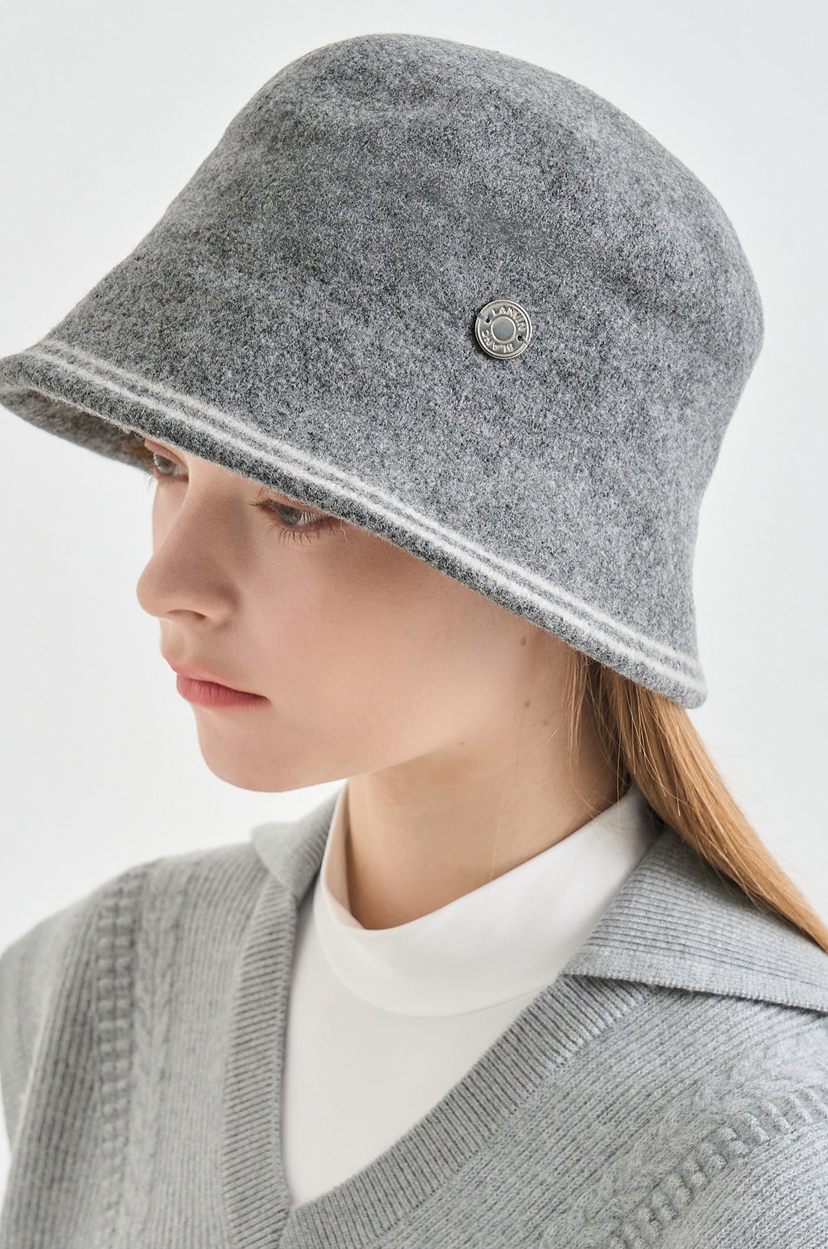 Person wearing a gray bucket hat with a button on a light gray background