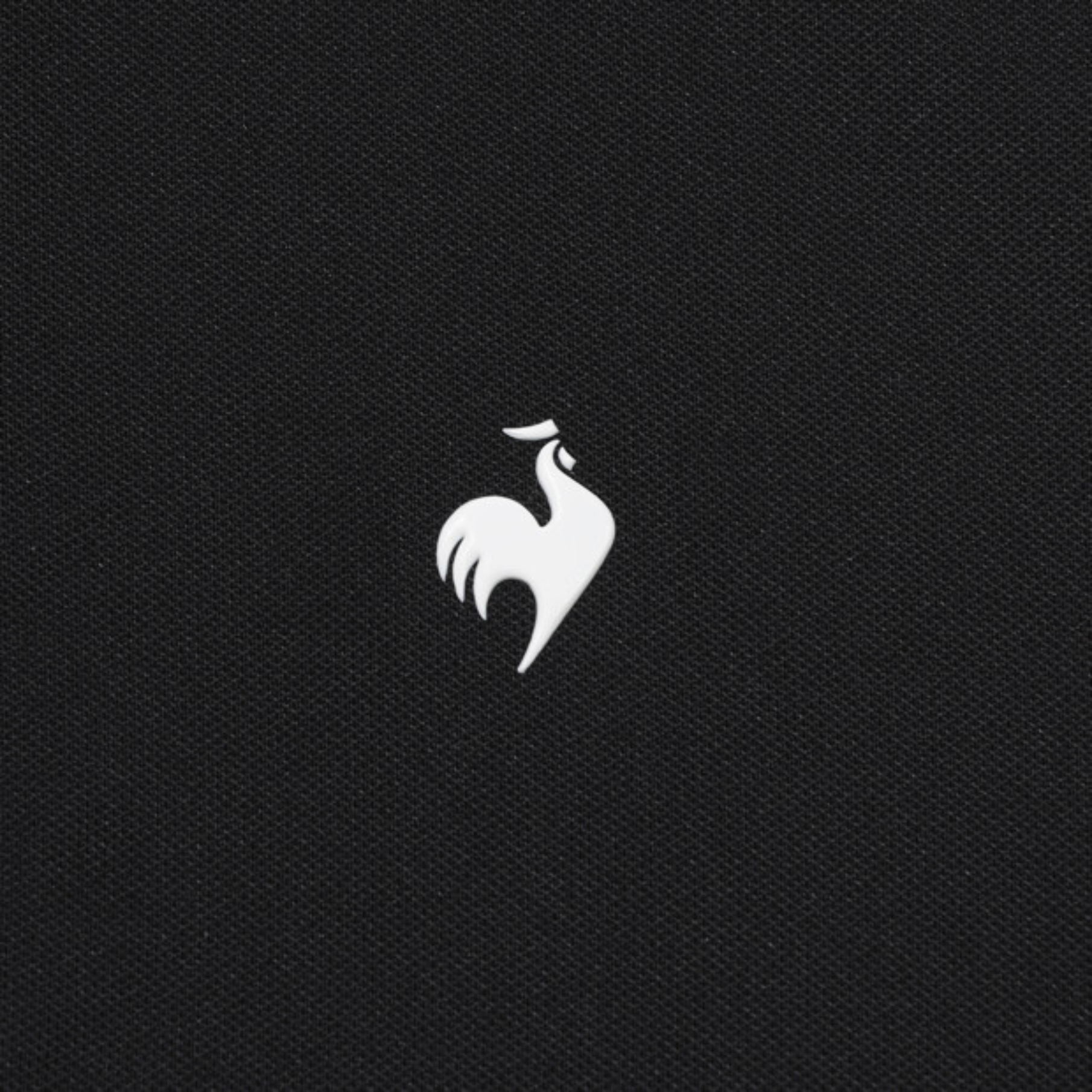 A close-up of a black textured fabric featuring the white embroidered logo of the French Rooster, representing the brand Gauloises.