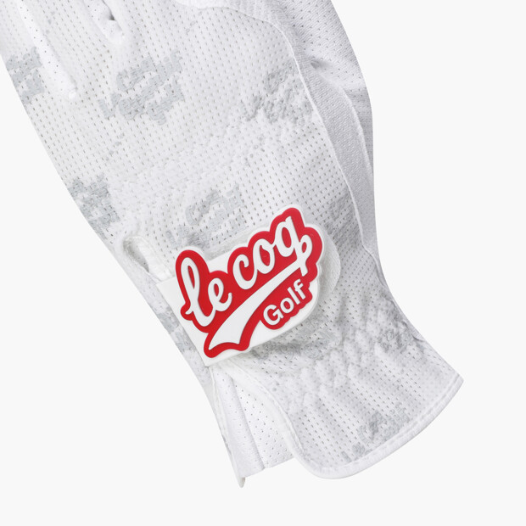 A close-up of a white perforated golf glove with a subtle gray camo pattern and a red and white 'le coq Golf' logo patch on the back.