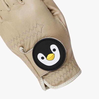 A close-up of a beige leather glove featuring a circular black patch with a white penguin face and yellow beak.