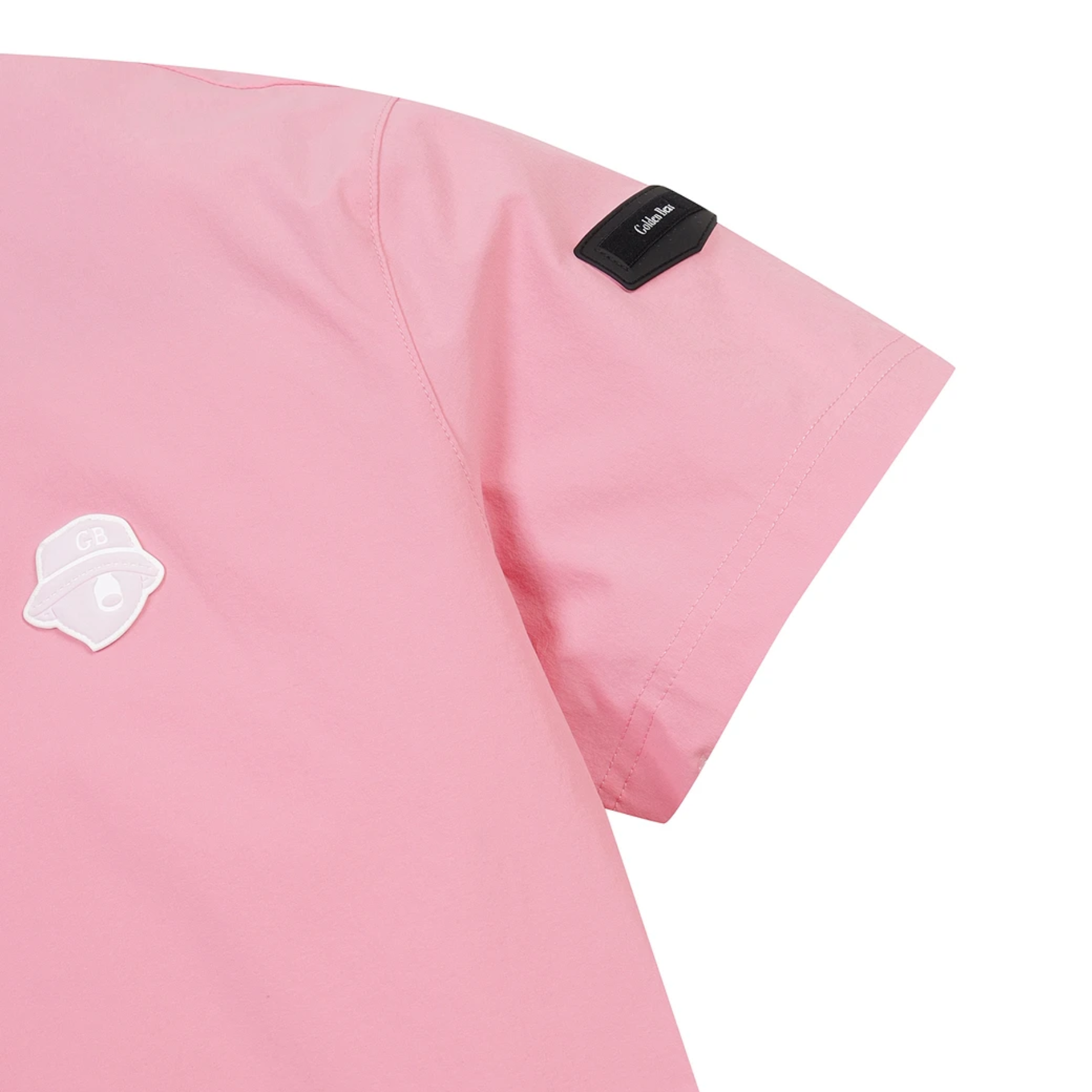 Close-up of a pink short-sleeve scrub top showing the shoulder, sleeve, and chest area with a small black brand tab and a white patch on a plain white background.