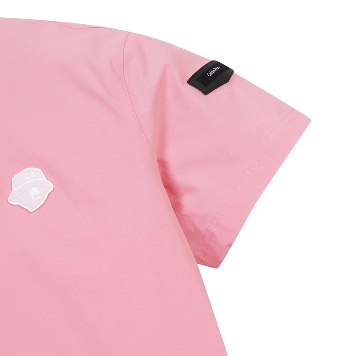 Close-up of a pink short-sleeve scrub top showing the shoulder, sleeve, and chest area with a small black brand tab and a white patch on a plain white background.