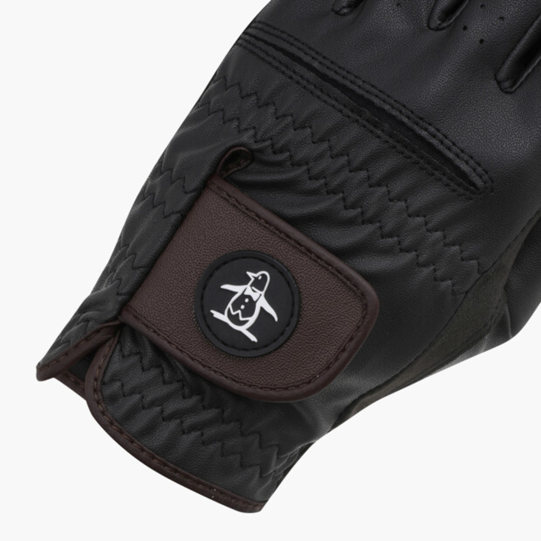 Close-up of a black winter glove with a brown wrist patch featuring a circular black logo with a white penguin skiing graphic, on a light gray background.