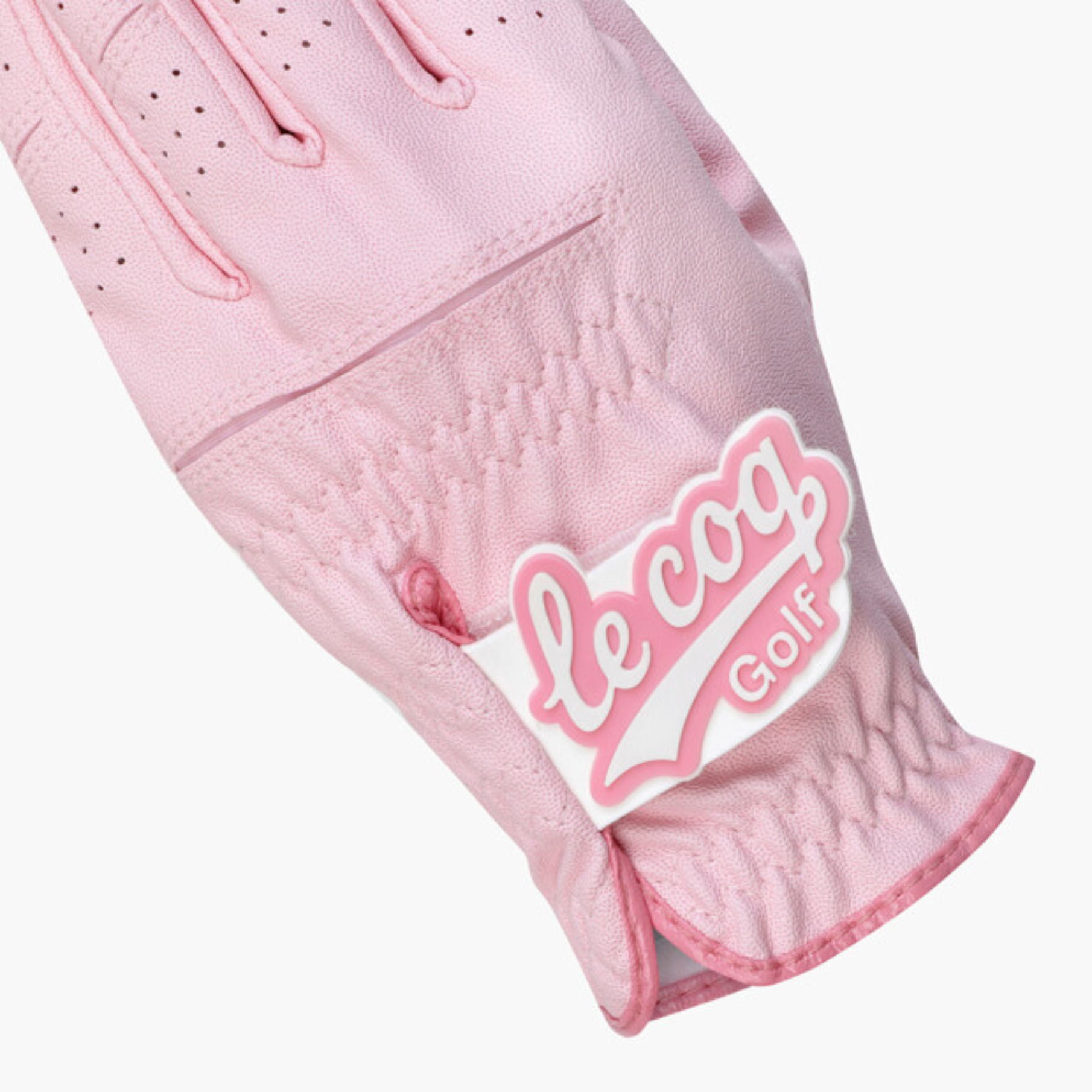 A close-up of a light pink golf glove with a white and pink 'le coq Golf' logo patch on the back of the hand, set against a plain light gray background.