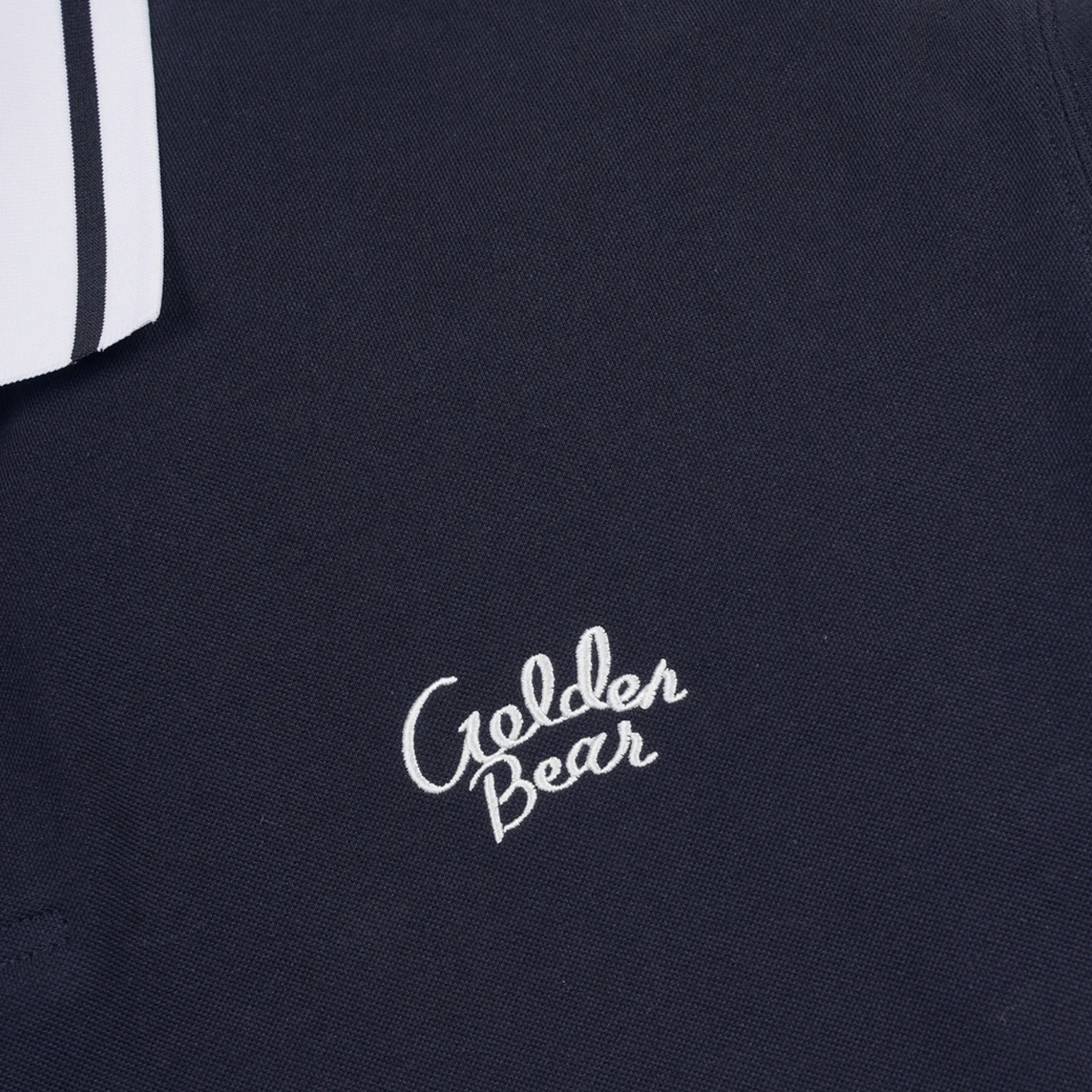 Close-up of a dark navy knit garment with white embroidered 'Golden Bear' script on the chest and a partial white sleeve with two black stripes visible at the upper left.