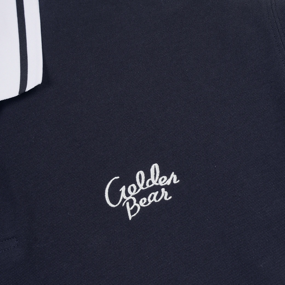 Close-up of a dark navy knit garment with white embroidered 'Golden Bear' script on the chest and a partial white sleeve with two black stripes visible at the upper left.