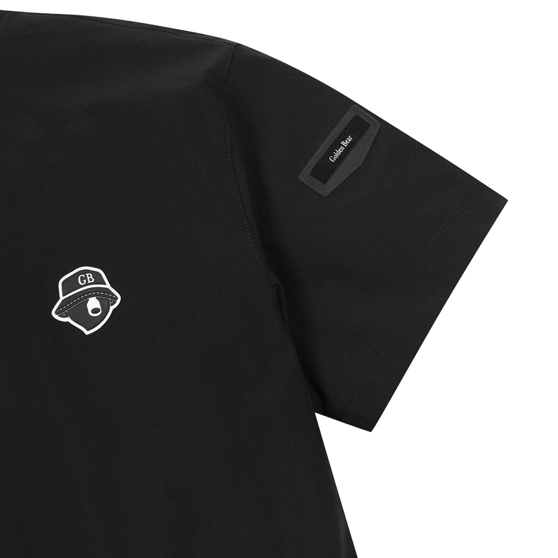 Close-up of a black short-sleeve t-shirt showing the left chest with a white outlined GB logo and a black rectangular patch on the sleeve with the text 'Golden Bear.