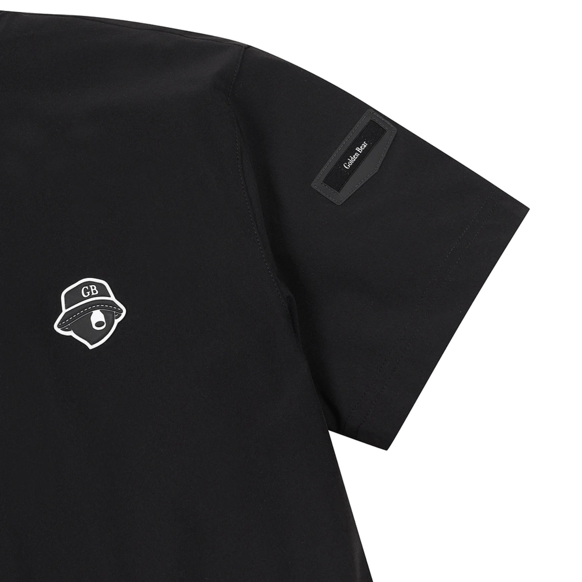 Close-up of a black short-sleeve t-shirt showing the left chest with a white outlined GB logo and a black rectangular patch on the sleeve with the text 'Golden Bear.