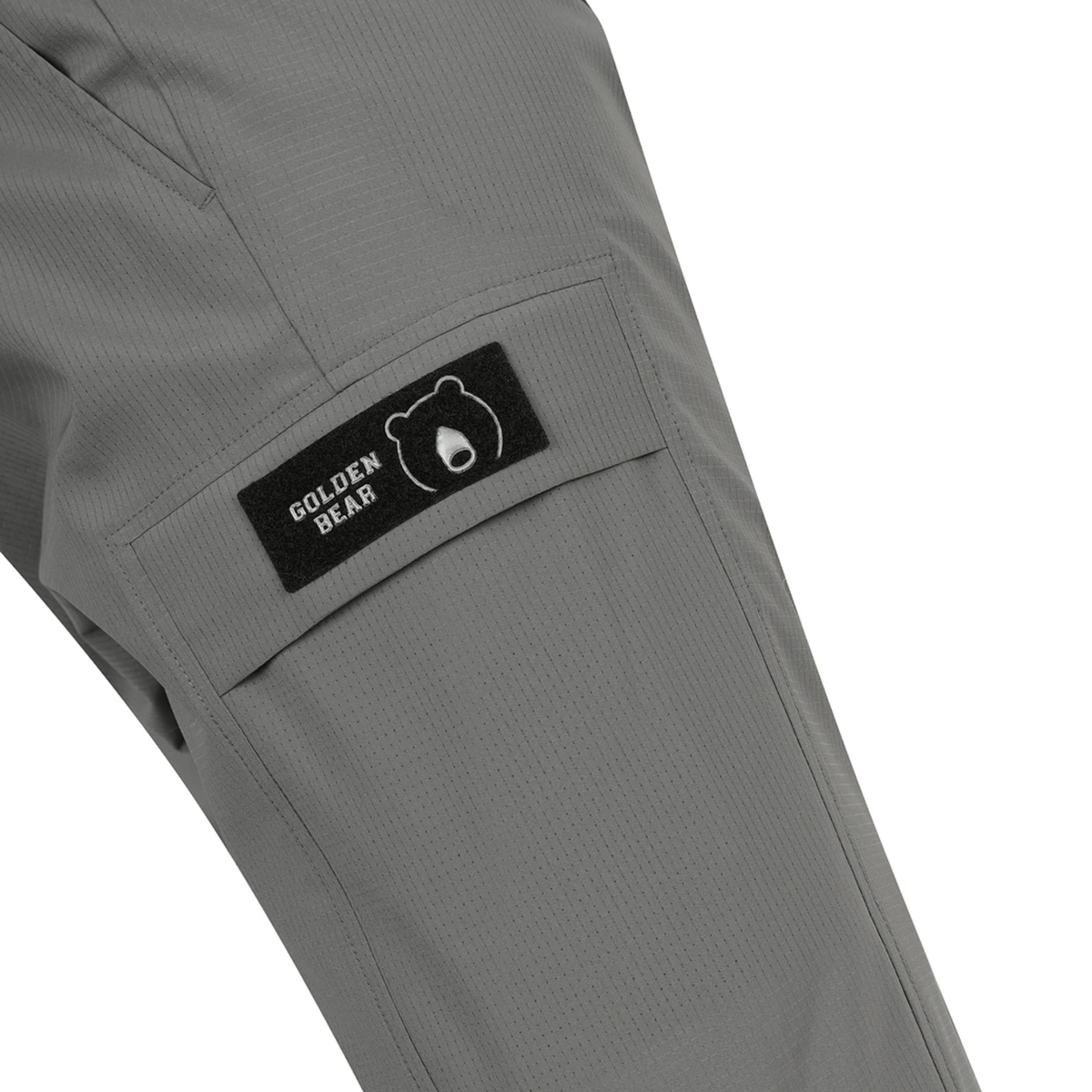 Close-up of gray pants showing a side pocket with a black Golden Bear brand patch on a white background.