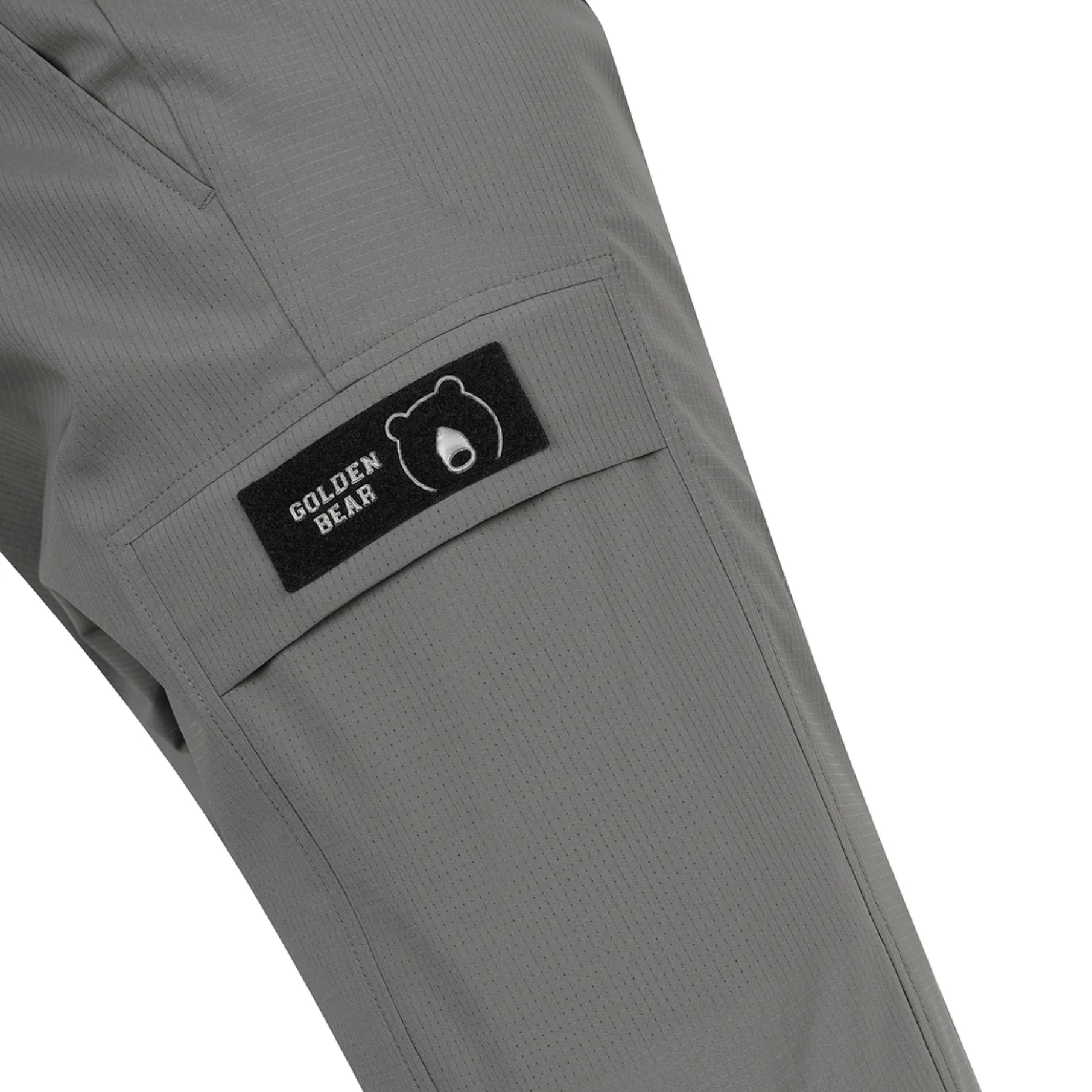 Close-up of gray pants showing a side pocket with a black Golden Bear brand patch on a white background.
