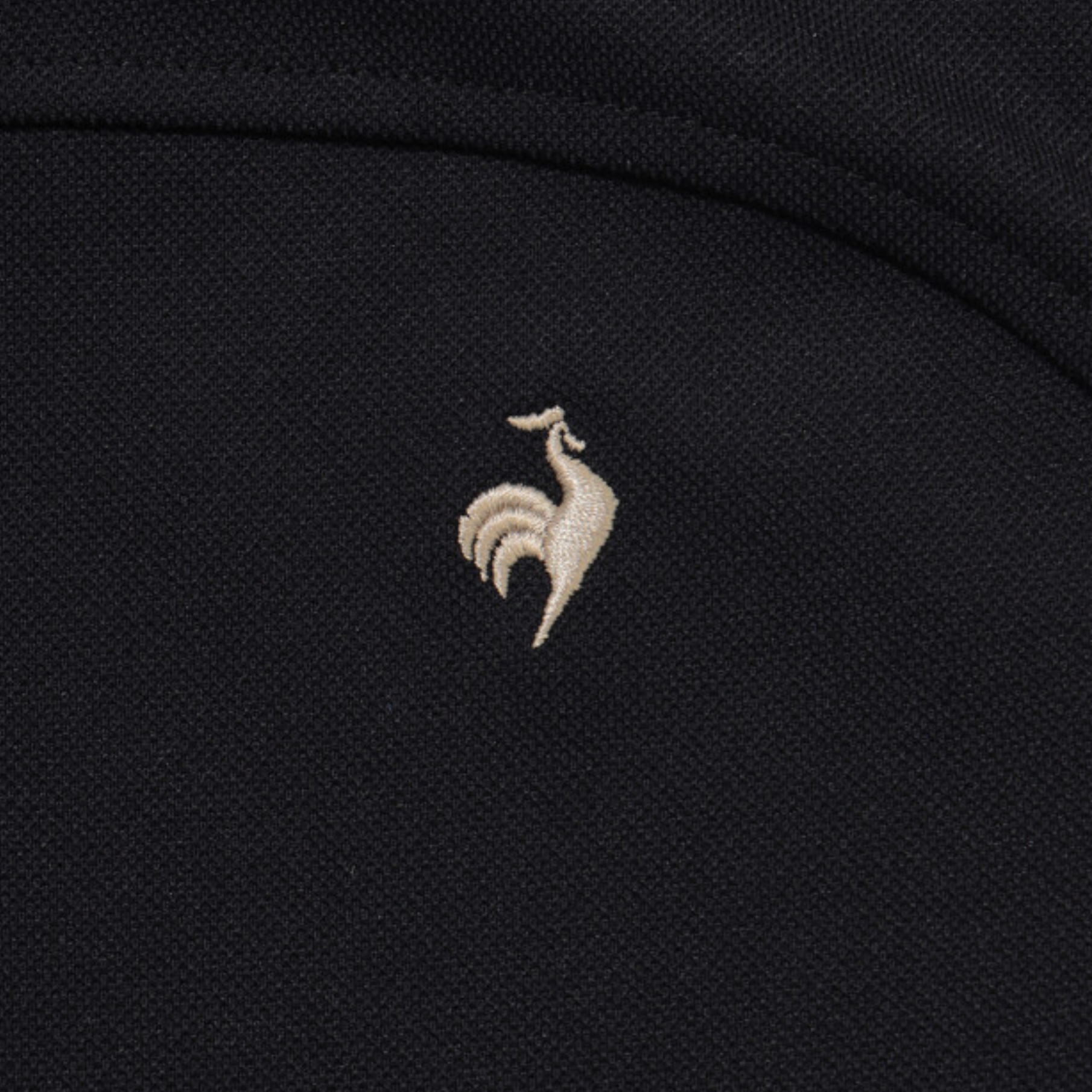 Close-up of a black textured fabric with a small beige embroidered rooster logo centered on the chest.