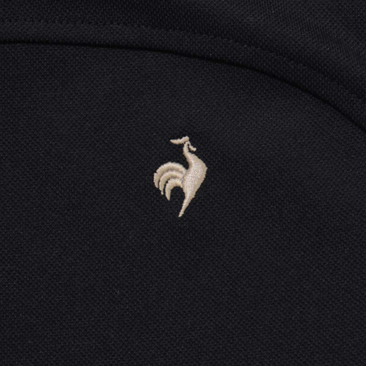 Close-up of a black textured fabric with a small beige embroidered rooster logo centered on the chest.