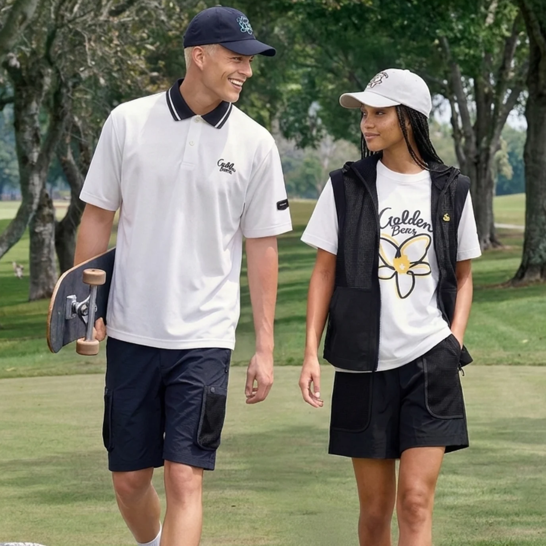 A man and a woman walking on a golf course wearing matching white and black golf apparel from the brand Goldton Golf.