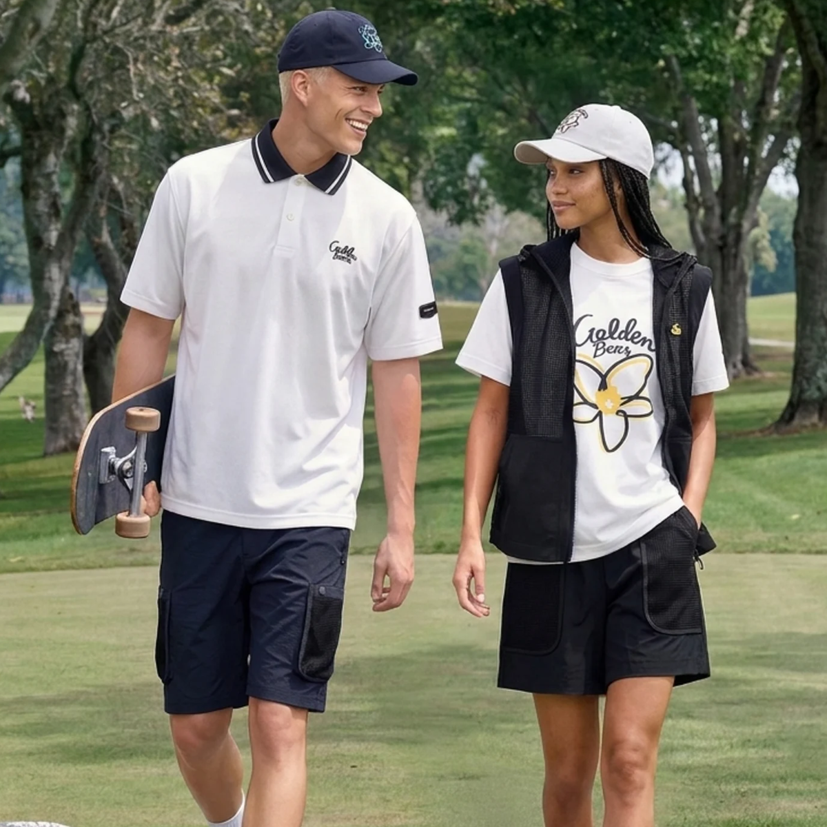 A man and a woman walking on a golf course wearing matching white and black golf apparel from the brand Goldton Golf.