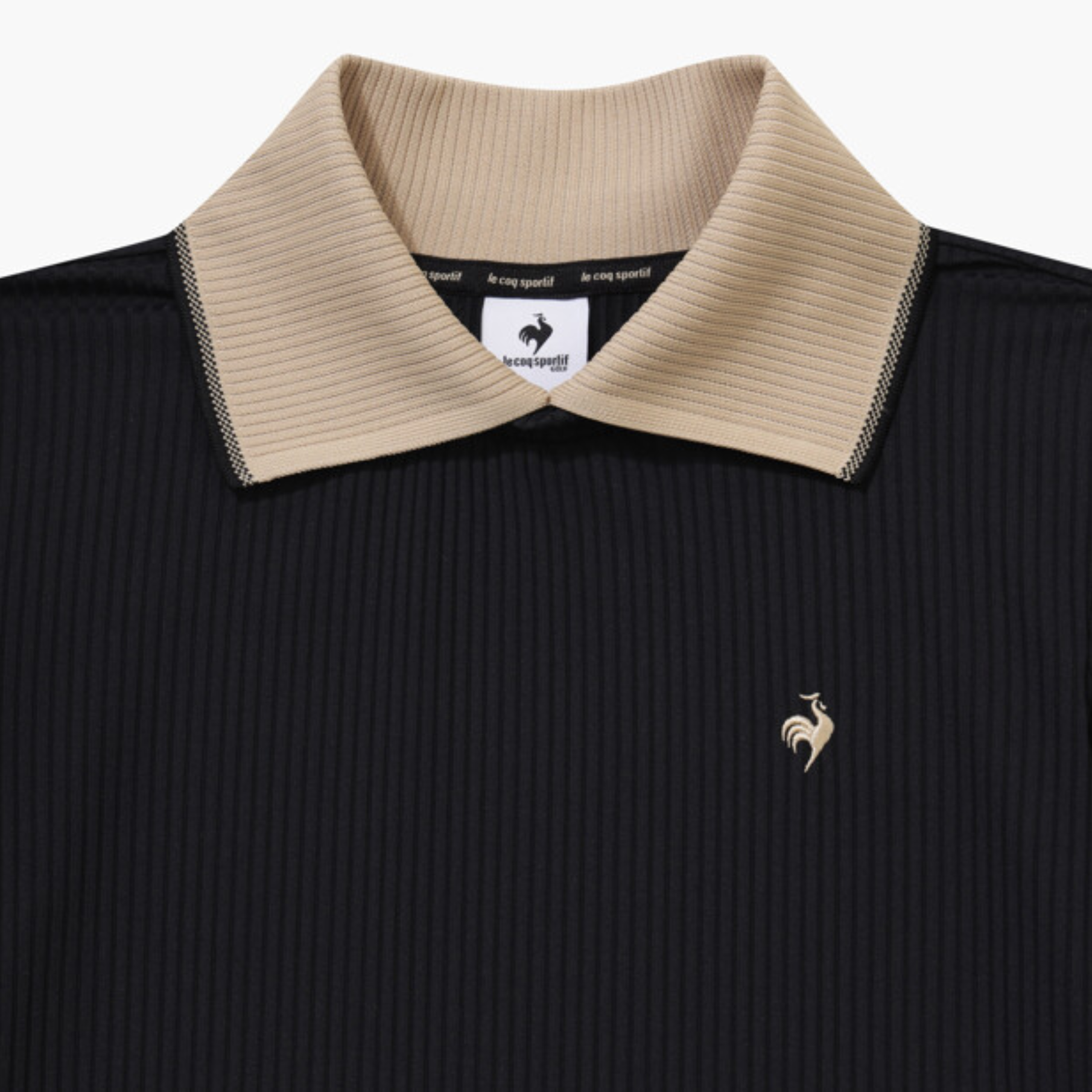 Close-up of a black ribbed polo shirt with a beige collar and a small gold rooster logo on the chest, showing the Le Malle brand label inside the collar.