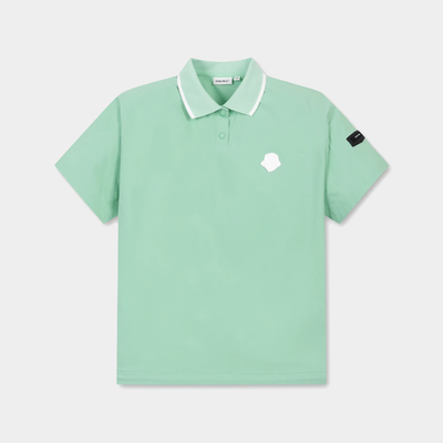 A mint green short-sleeve polo shirt with a white collar, featuring a small white logo on the left chest and a black brand patch on the right sleeve, displayed on a light gray background.