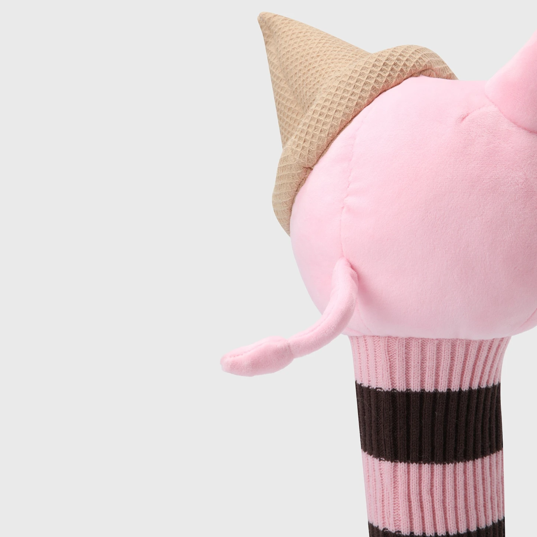 Close-up of a pink plush toy shaped like a pig wearing a tan waffle-cone hat, with a pink and dark brown striped ribbed lower section, on a light gray background.