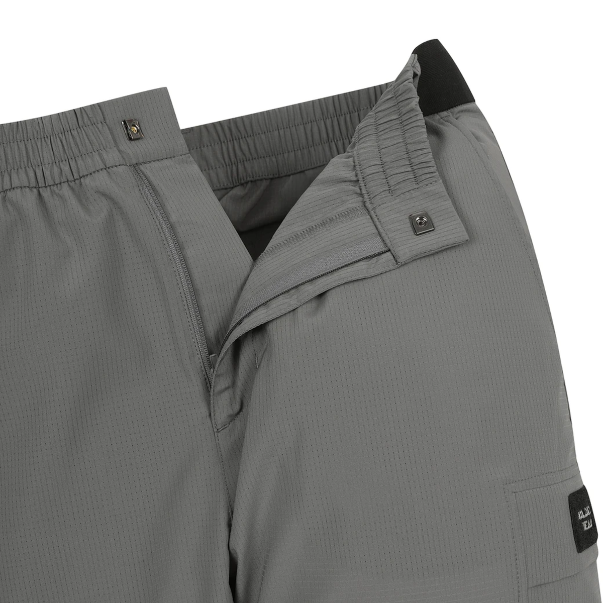 Close-up of gray technical outdoor pants showing the elastic waistband, reinforced pocket seam, and a small black brand patch on the lower leg.