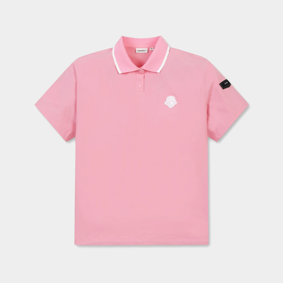 A pink short-sleeve polo shirt with a white contrast collar, featuring a small white geometric logo on the left chest and a black brand patch on the right sleeve, displayed on a light gray background.