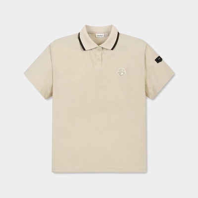 A light beige short-sleeve polo shirt with a black-trimmed collar and a small white embroidered shield logo on the left chest, displayed on a clean light gray background.