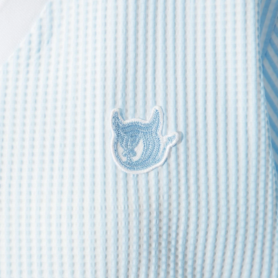 Close-up of embroidered chest logo on women's light blue seersucker golf polo.