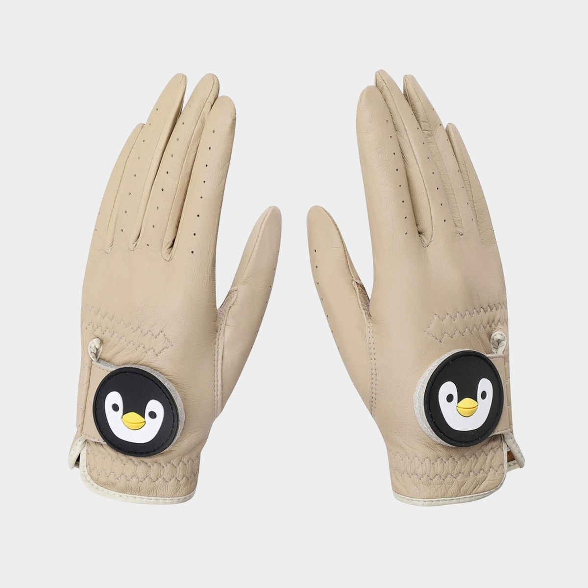 A pair of beige leather golf gloves with a circular penguin patch on the back of the hand, shown against a light gray background.
