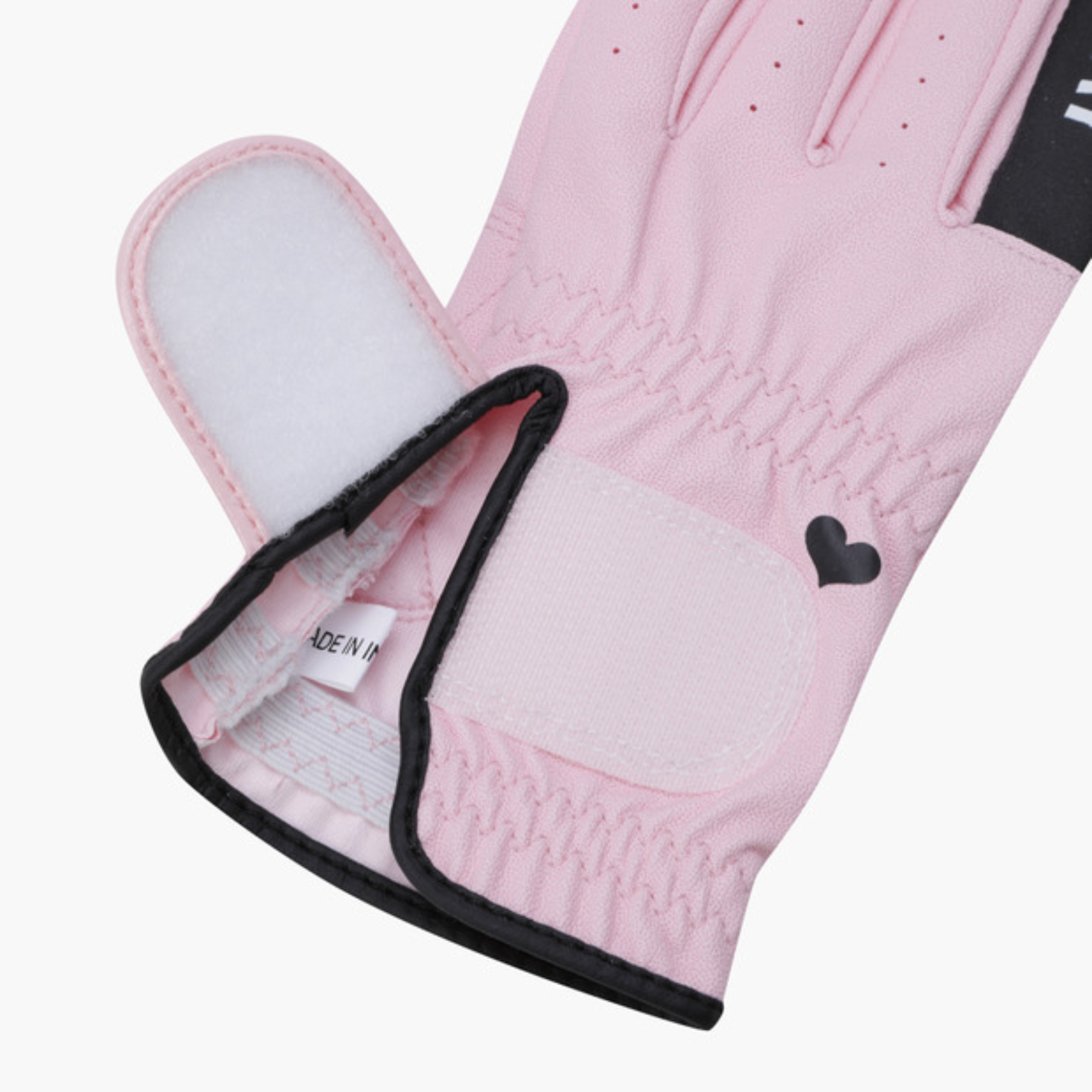 A close-up of a light pink golf glove with black trim, showing the back of the hand, a black heart logo, and the interior cuff with a white 'MADE IN' tag.