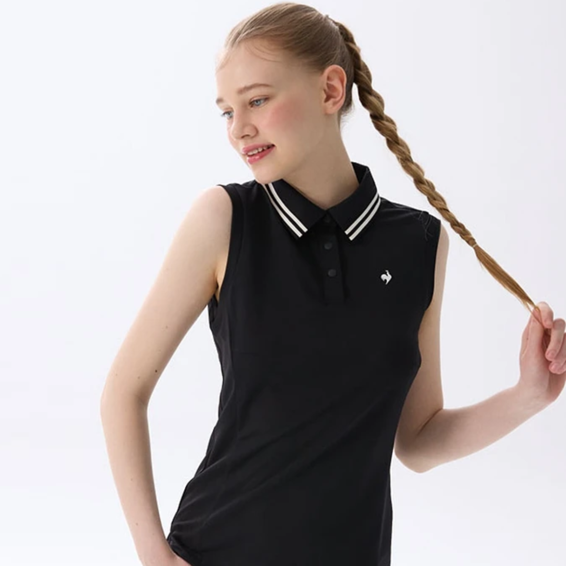 A young girl with a long braided ponytail wearing a black sleeveless polo shirt with a white and black striped collar, posed against a solid white background.