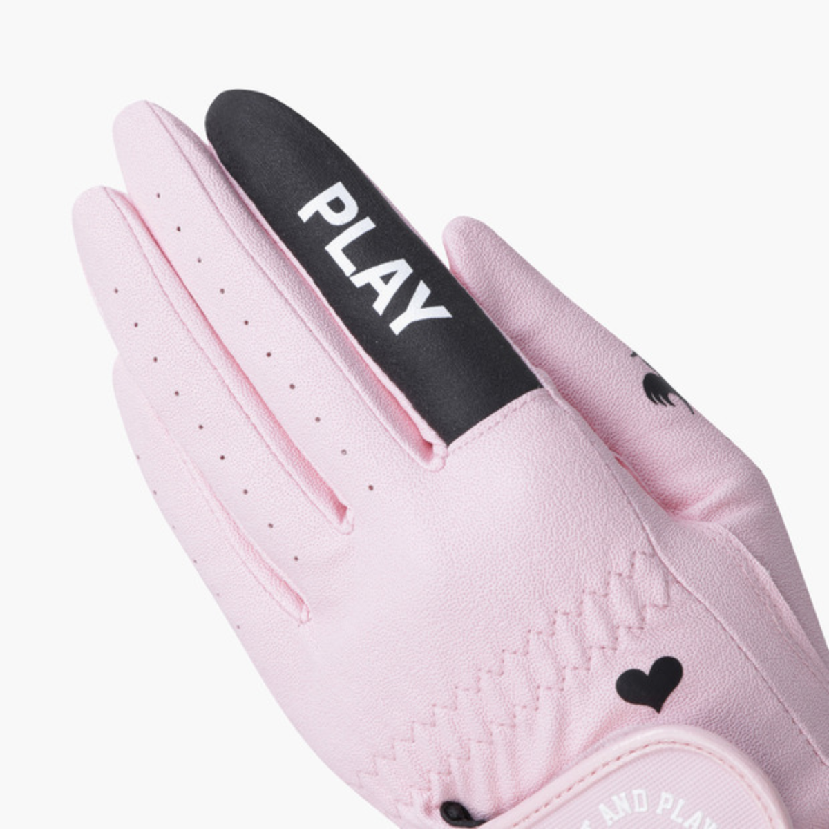 A close-up of a light pink golf glove with a black thumb strap featuring the white text 'PLAY'.