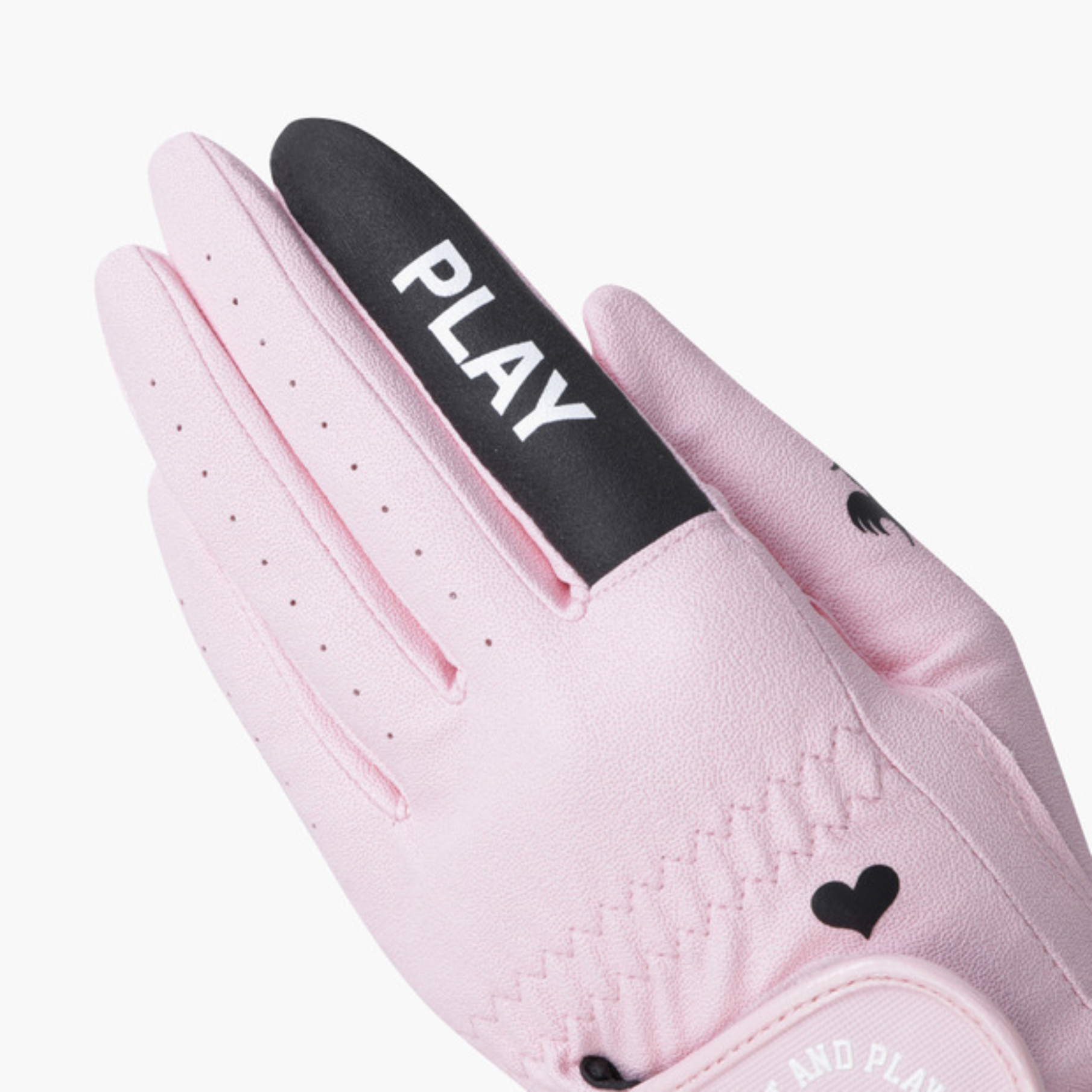 A close-up of a light pink golf glove with a black thumb strap featuring the white text 'PLAY'.