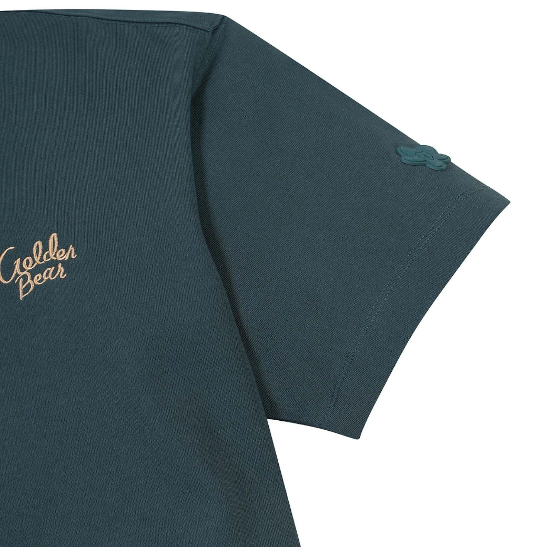 Close-up of a dark teal-green short-sleeve t-shirt showing the left chest area with a gold embroidered 'Golden Bear' logo and a small matching embroidered bear head on the sleeve cuff.