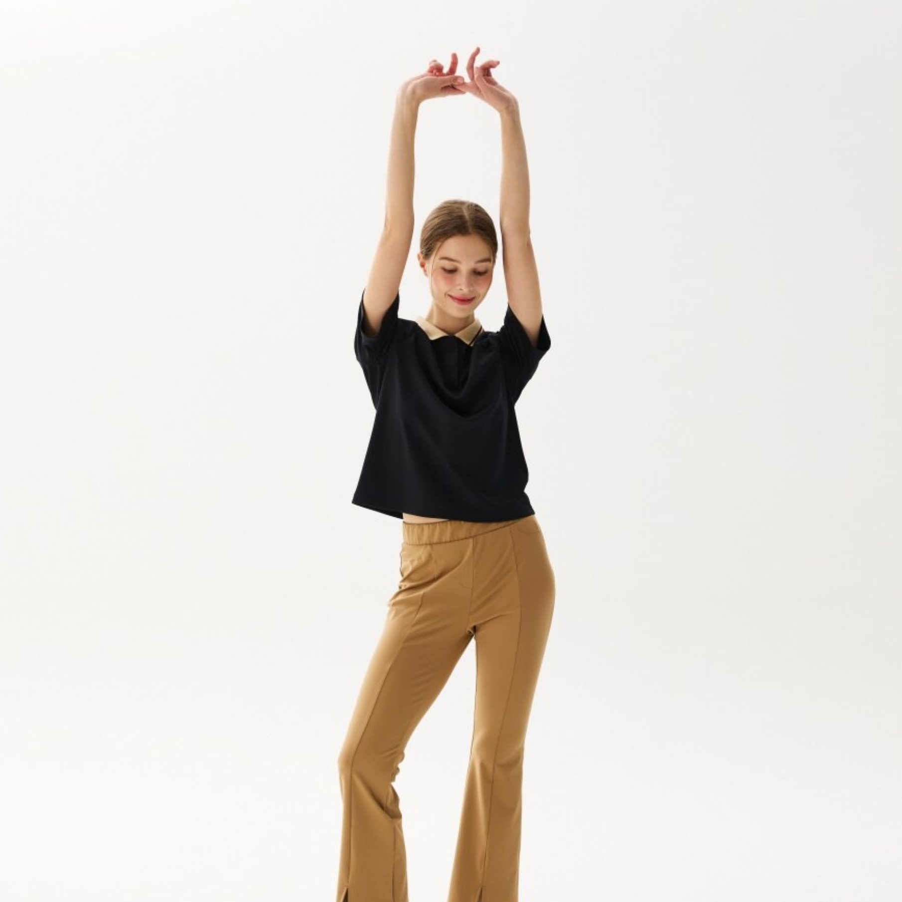 A woman modeling a black short-sleeve cowl-neck top and tan high-waisted flare pants against a plain white studio background.