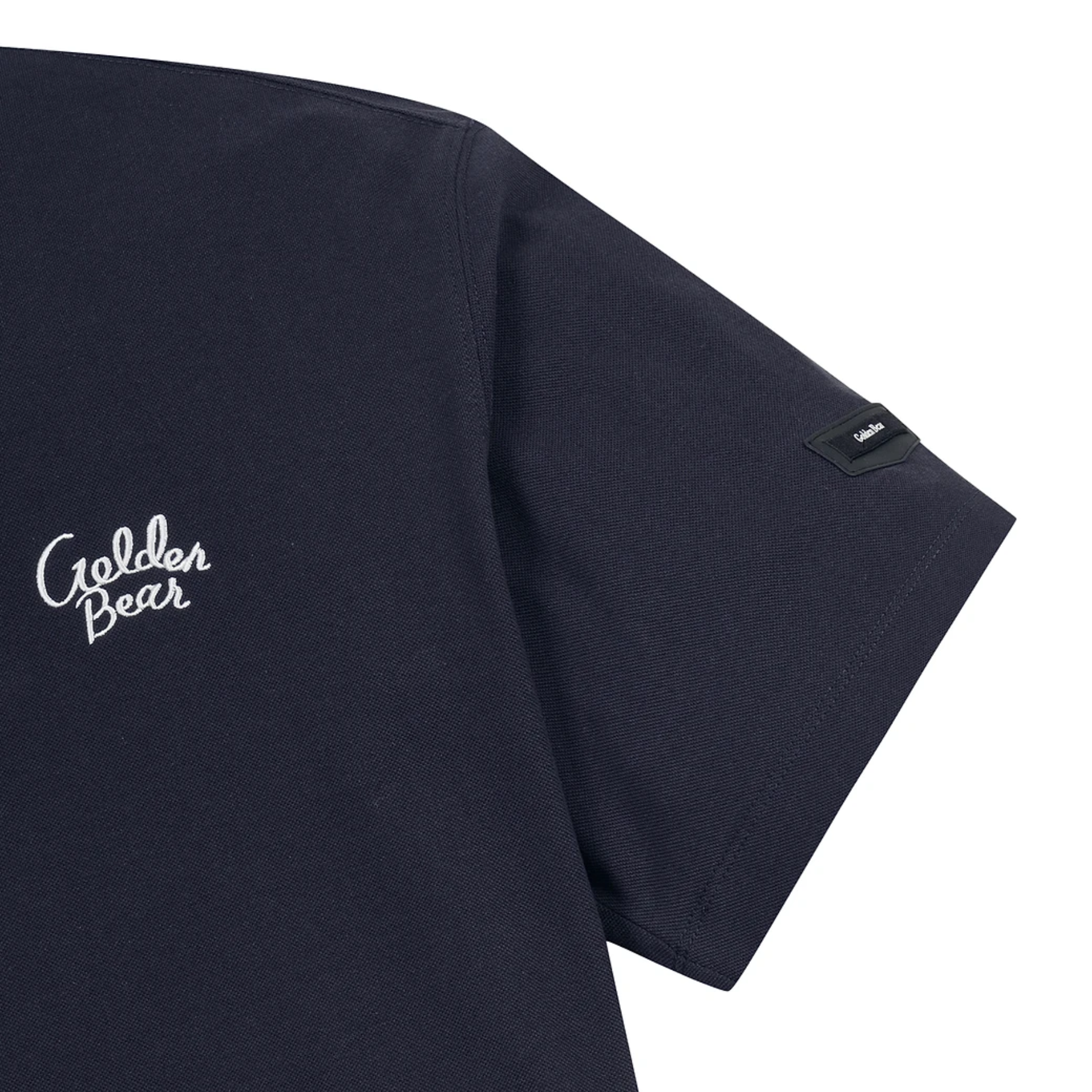 Close-up of a dark navy short-sleeve t-shirt showing the left chest with white embroidered 'Golden Bear' script and a small black brand tab on the sleeve, set against a plain white background.