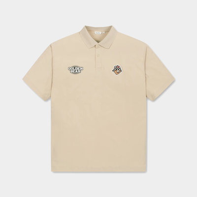 A beige short-sleeve polo shirt with a two-button placket, featuring a 'GOLDEN BEAR' patch on the left chest and a small mascot patch on the right chest, displayed on a light gray background.
