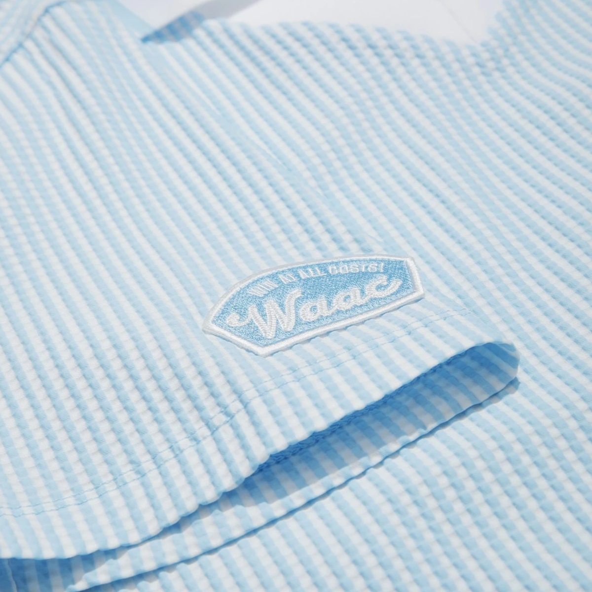 Close-up of sleeve logo patch on women's light blue seersucker golf polo.