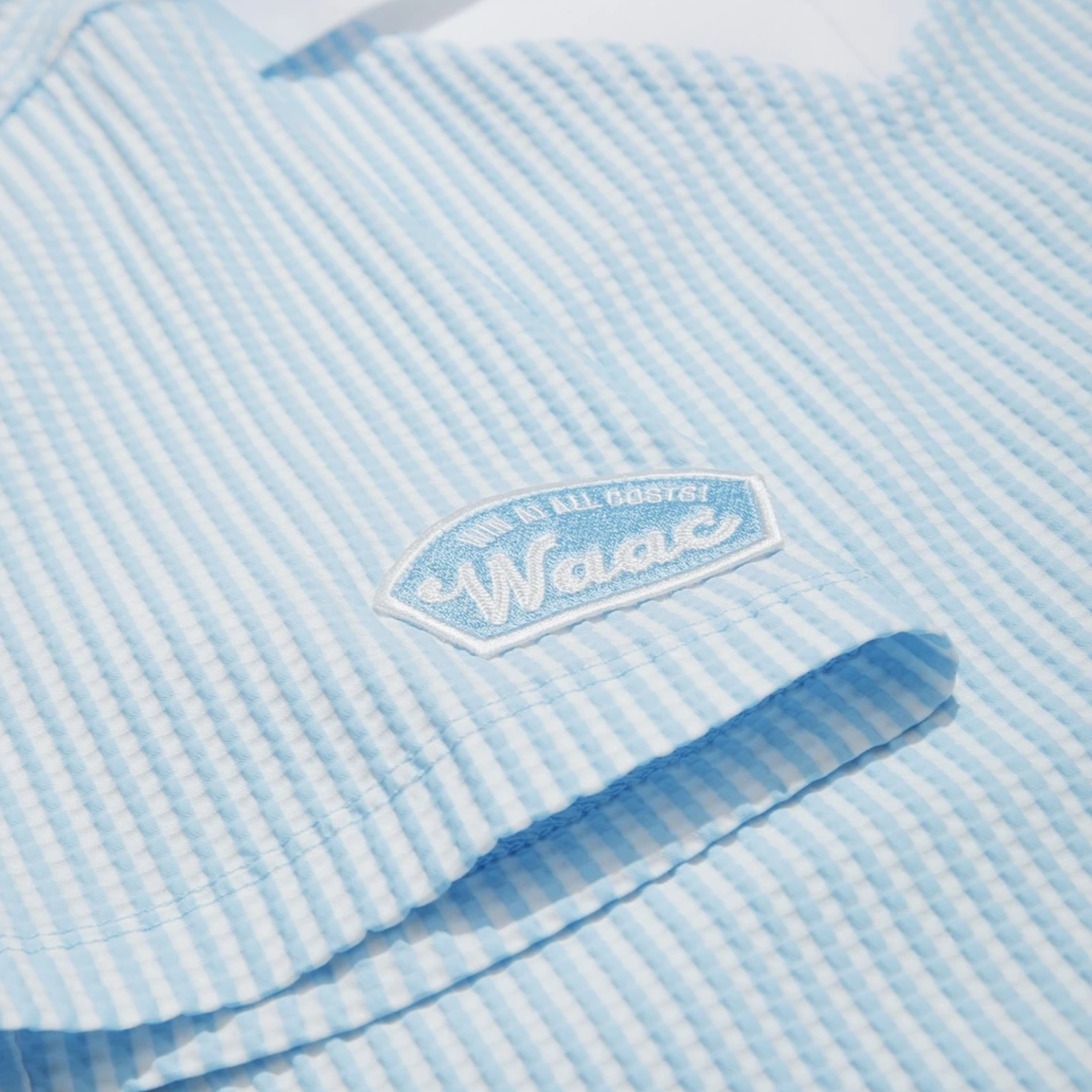 Close-up of sleeve logo patch on women's light blue seersucker golf polo.