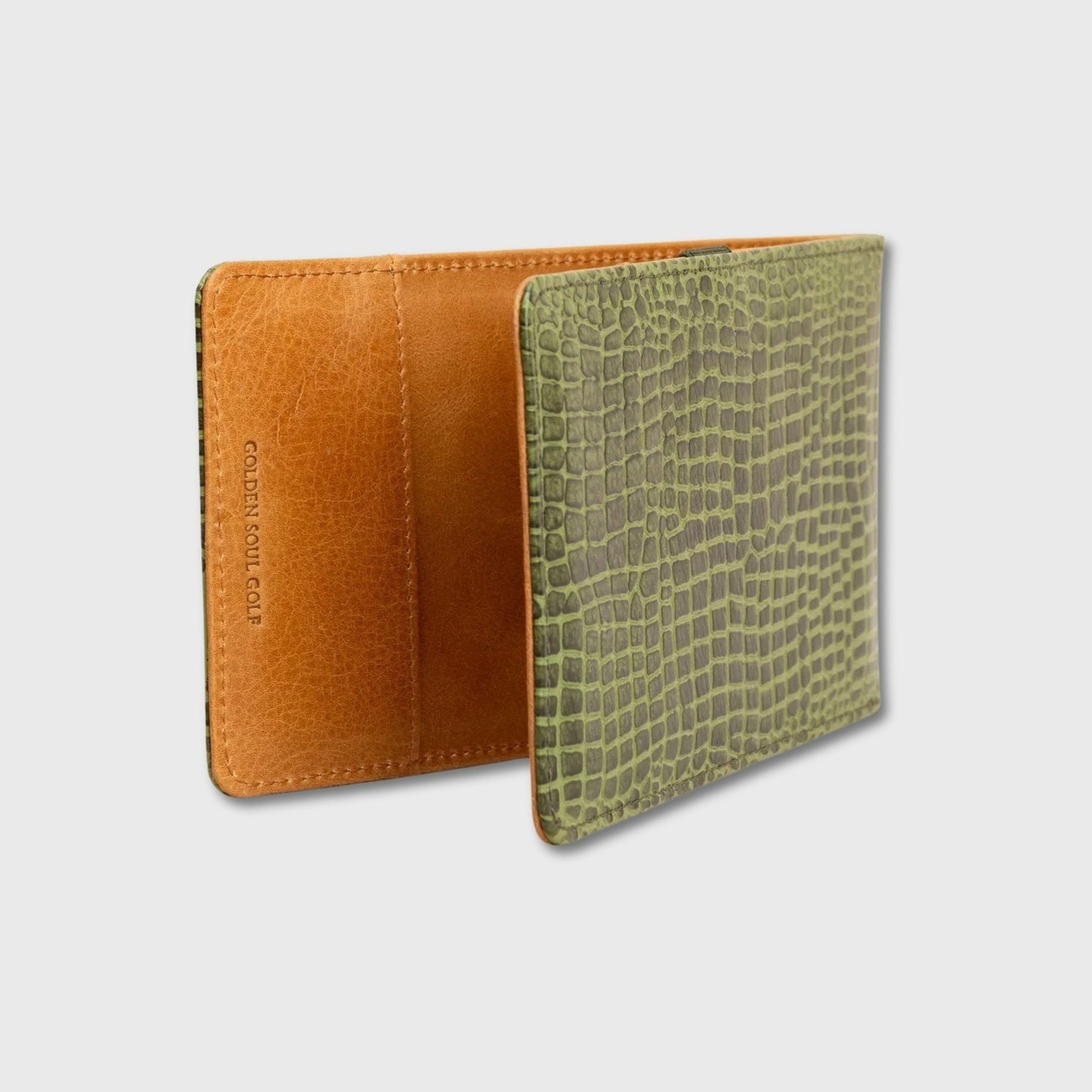 A yardage book holder shown open against a light gray background, featuring a tan interior and an olive green crocodile-embossed exterior.