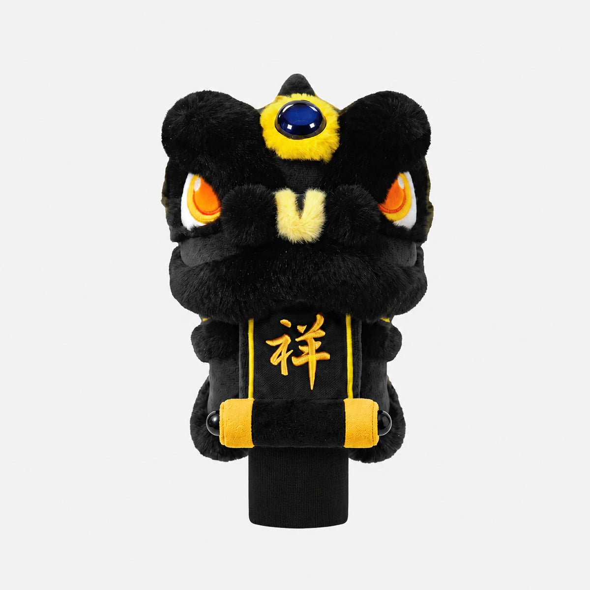 A black plush lion head accessory with yellow and gold accents, orange eyes, and a blue gem on the forehead, mounted on a black cylindrical stand against a light gray background.