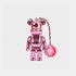 A metallic pink Bearbrick keychain featuring a shiny pink bear figure with a pink donut charm hanging from a multicolor braided cord. The donut charm is decorated with colorful sprinkles and the word &