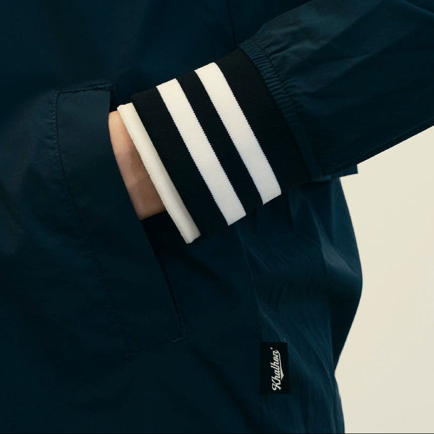 A three-panel collage showing a dark navy varsity-style jacket from different angles. The top panel shows a model wearing the jacket with beige pants in an indoor setting.
