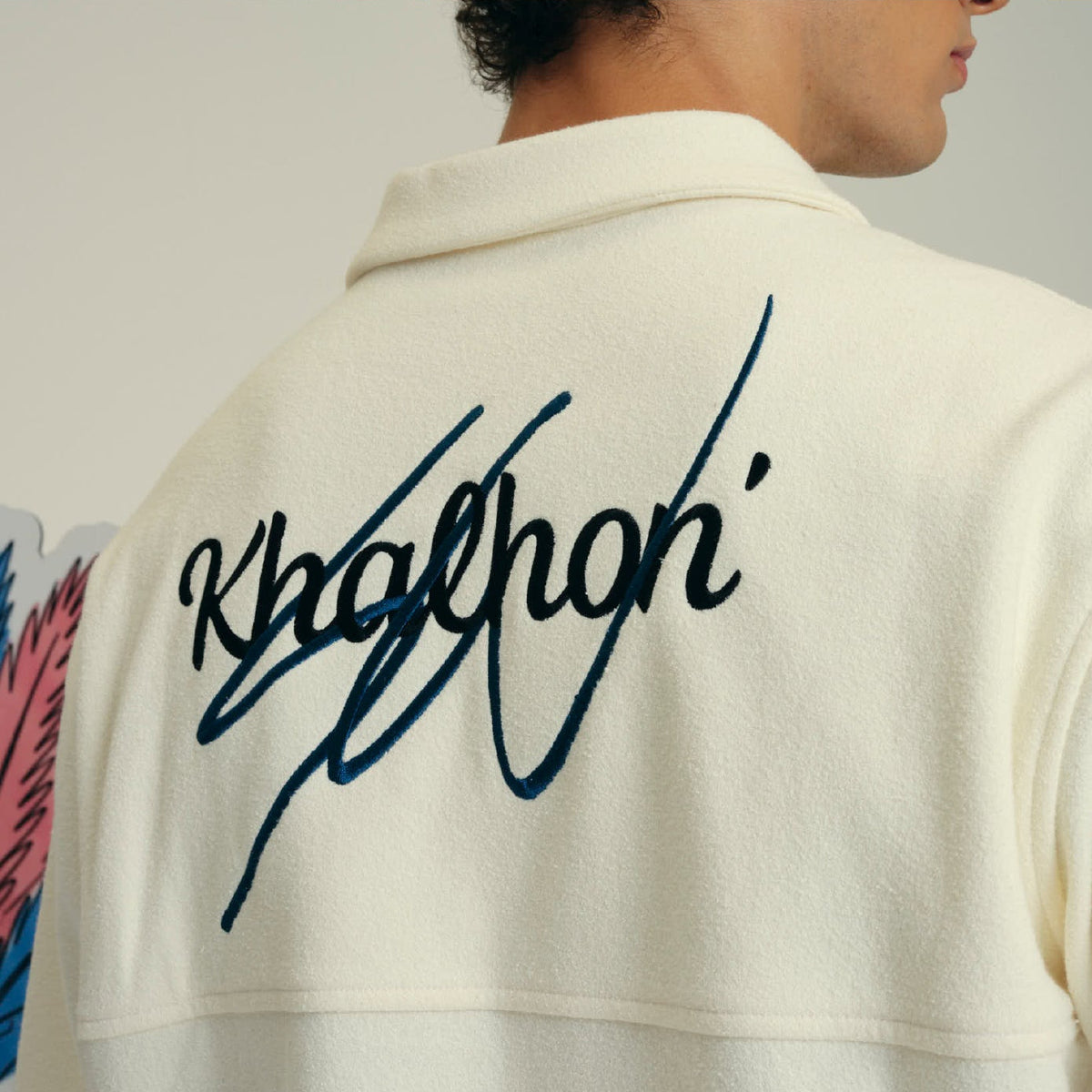 Close-up back view of a person wearing an off-white fleece pullover with a large black script logo reading 'Khaklon' across the upper back.