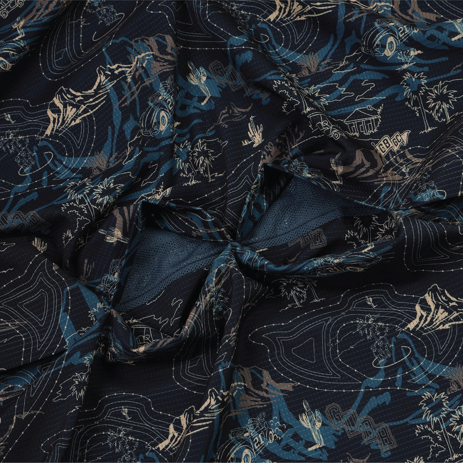 A close-up of draped fabric with a dark navy base and an intricate light beige and blue scenic pattern featuring mountains, waves, and traditional architectural details.