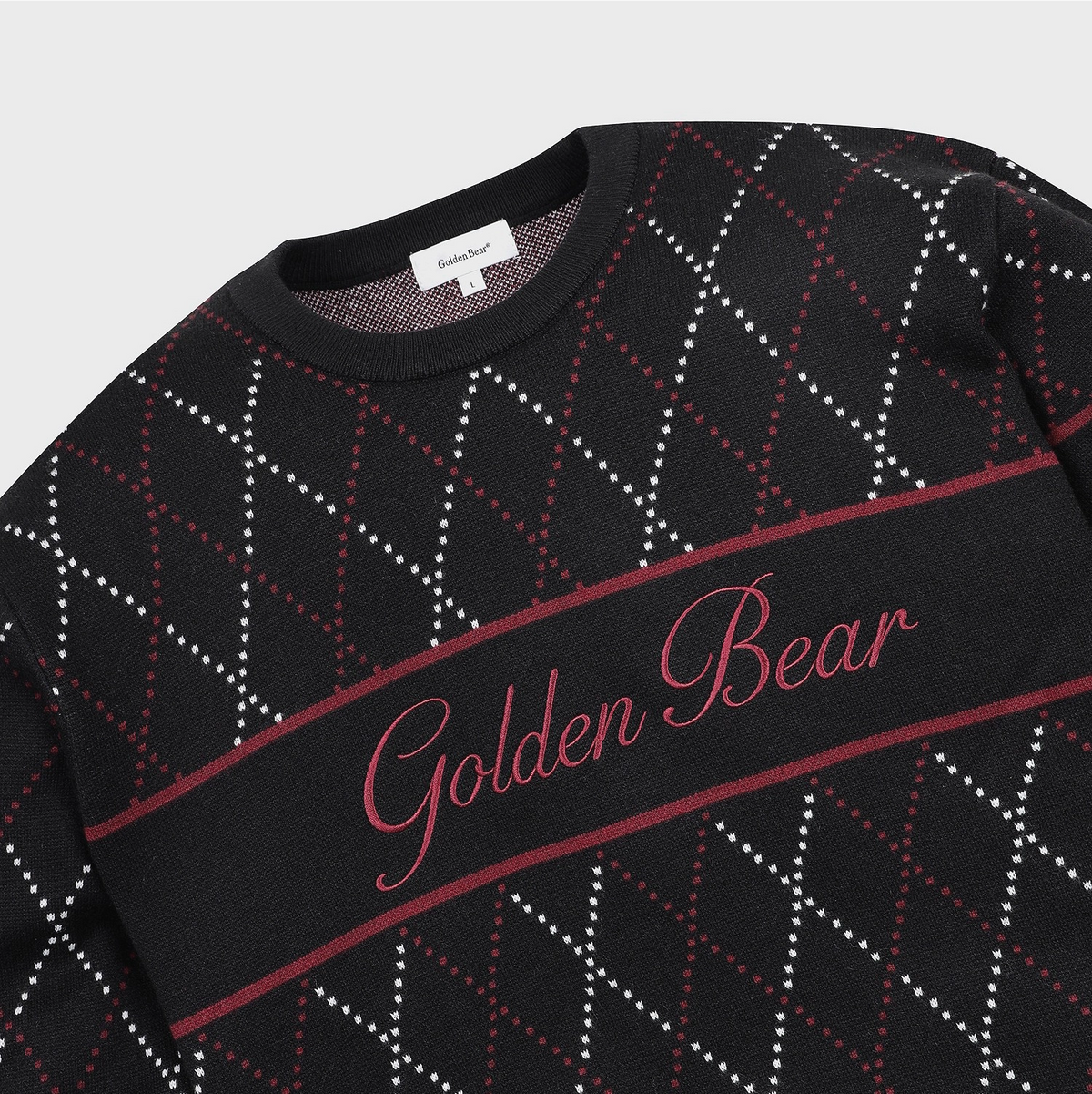 A close-up of a black crewneck sweater featuring a red and white argyle pattern and a central horizontal band with 'Golden Bear' embroidered in red script.