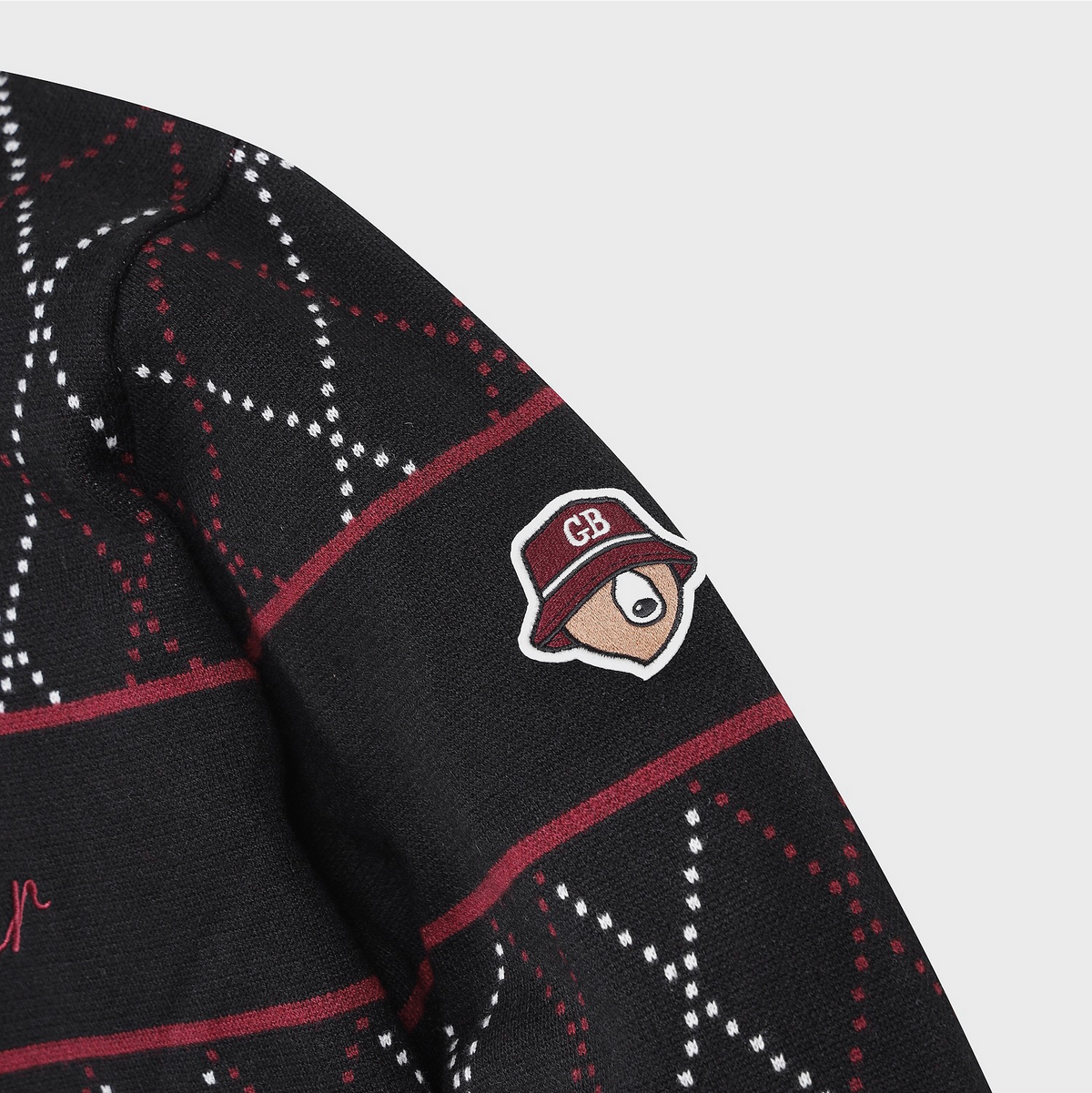 Close-up of a black knit sweater with a red and white argyle pattern and a small embroidered CB logo patch on the sleeve.