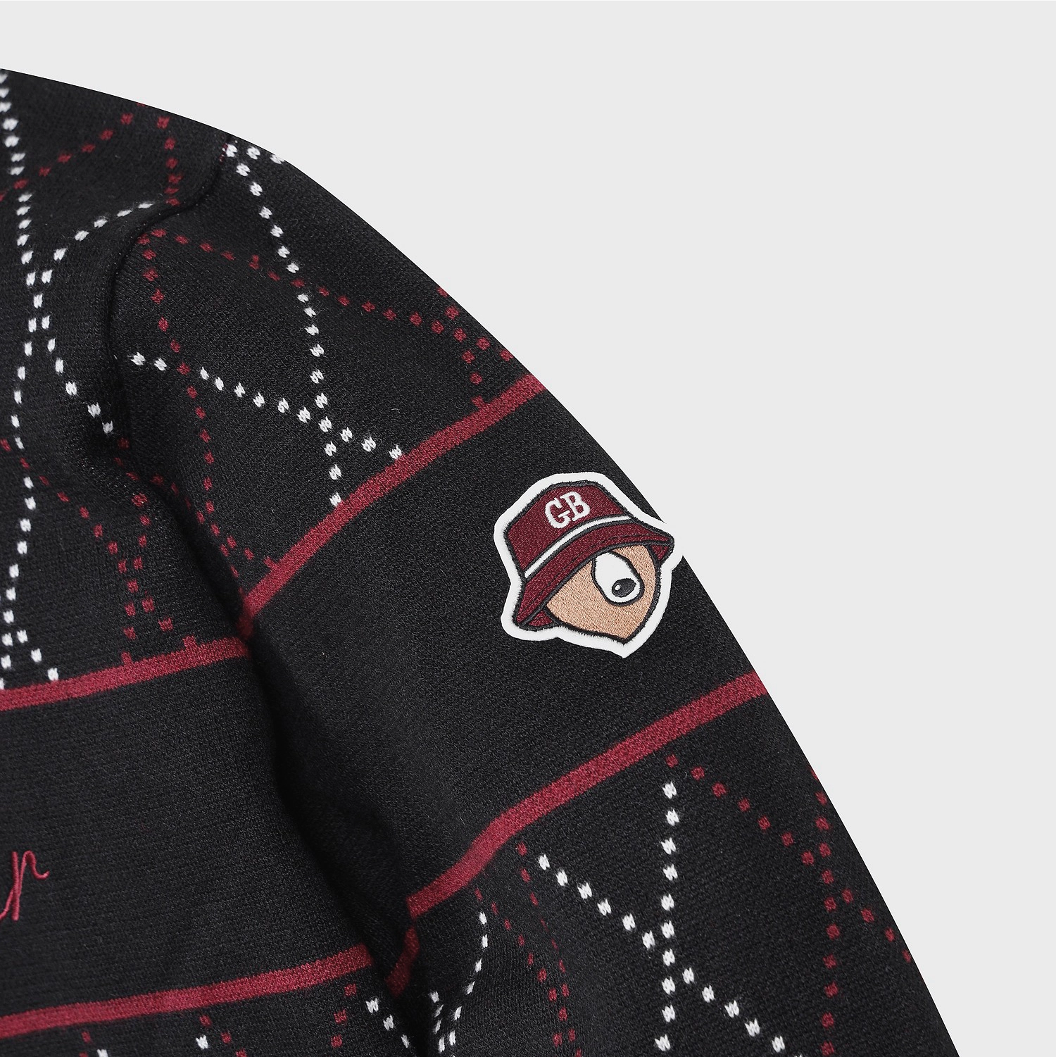 Close-up of a black knit sweater with a red and white argyle pattern and a small embroidered CB logo patch on the sleeve.