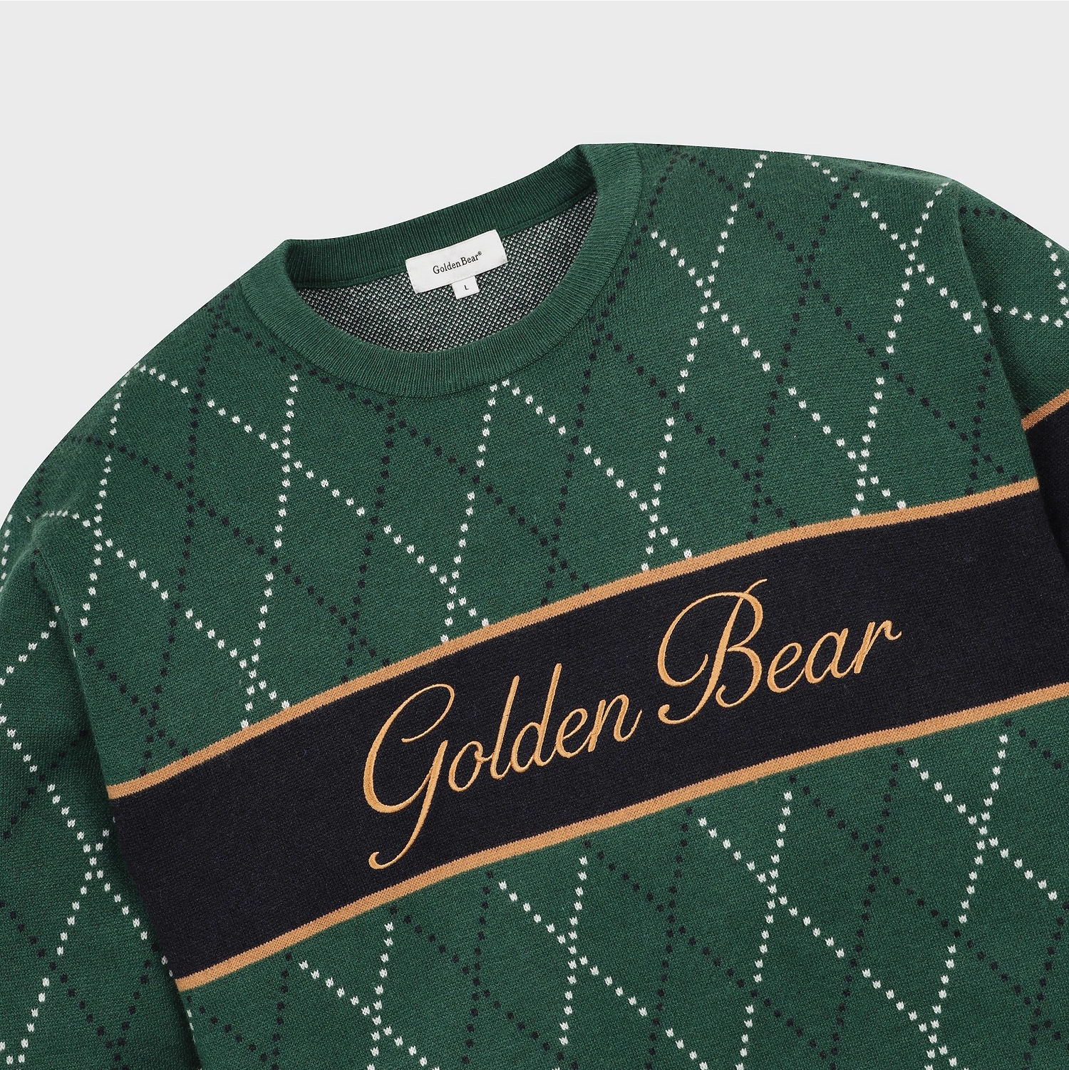 A close-up of a green crewneck sweater with a black and white argyle pattern, featuring a wide black horizontal stripe across the chest with 'Golden Bear' written in gold script.