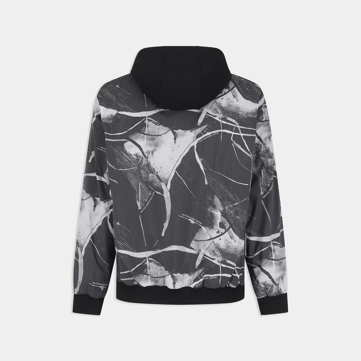 A black and white abstract paint splatter print hoodie shown from the back, featuring a solid black hood and ribbed cuffs and hem, set against a light gray background.