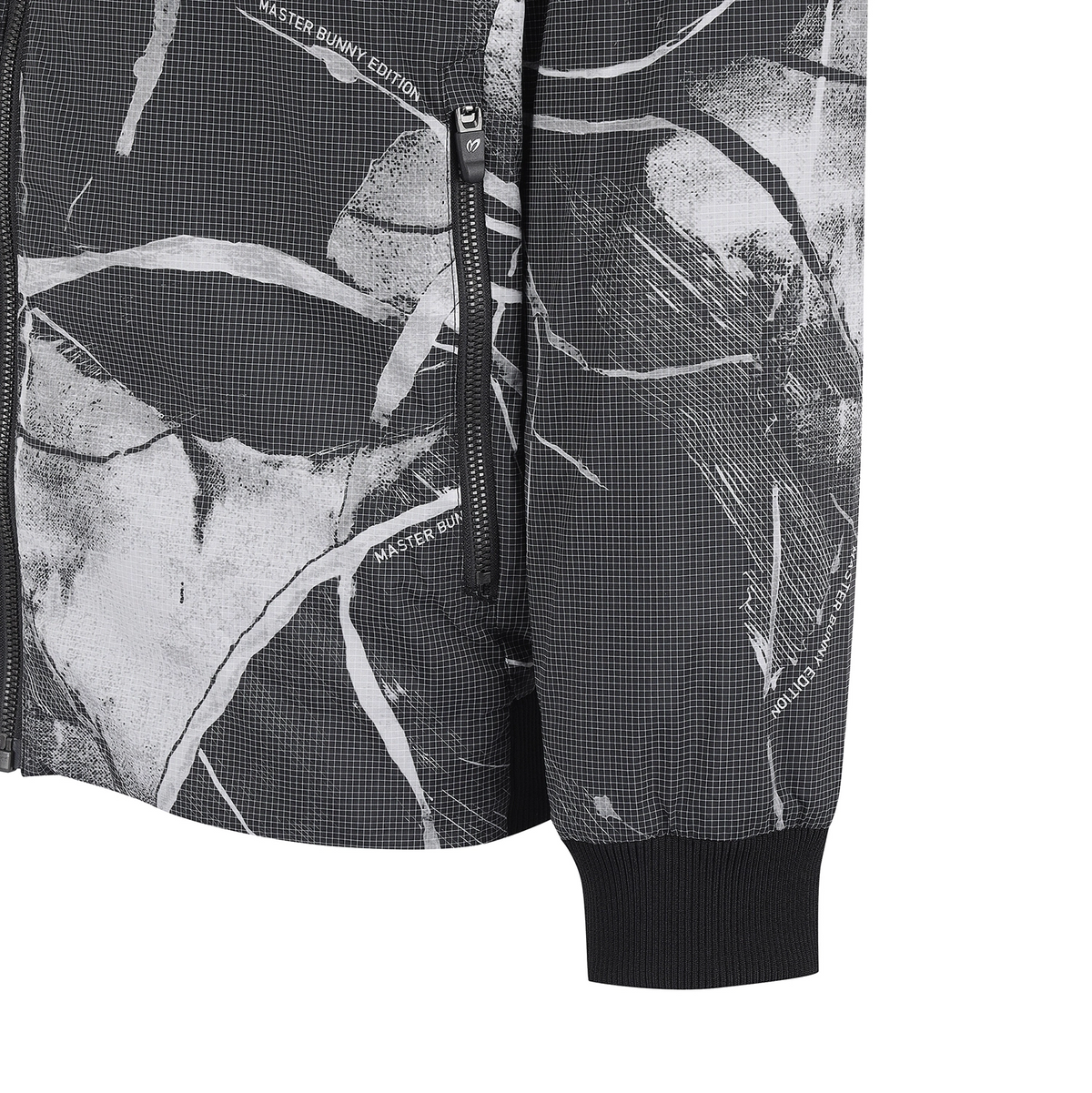 Close-up of a black and white abstract patterned jacket with a ribbed black cuff and a vertical zipper pocket.