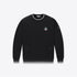 A black crewneck sweatshirt with white contrast trim on the collar, cuffs, and hem, featuring a small embroidered graphic on the left chest and a small patch on the right sleeve, displayed against a light gray background.